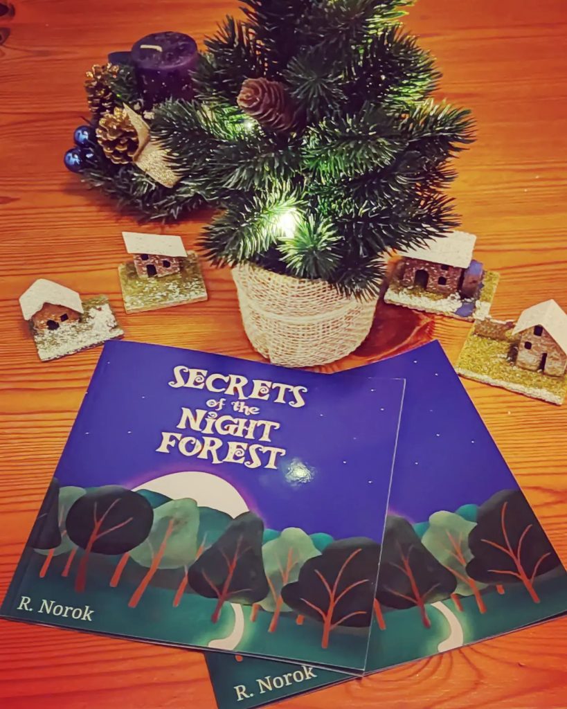 Two copies of the book Secrets of the Night Forest in front of a winter diorama.